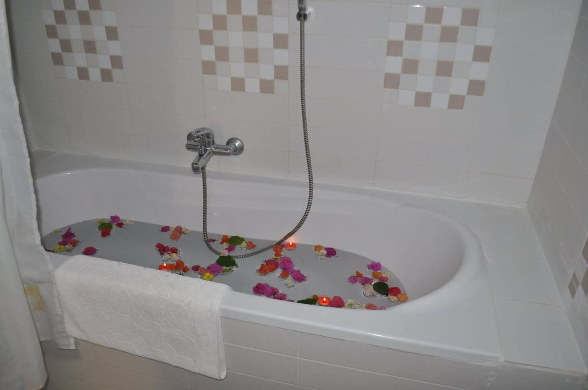 Une baignoire équipée d’un pommeau de douche, entourée de fleurs flottantes et de bougies.