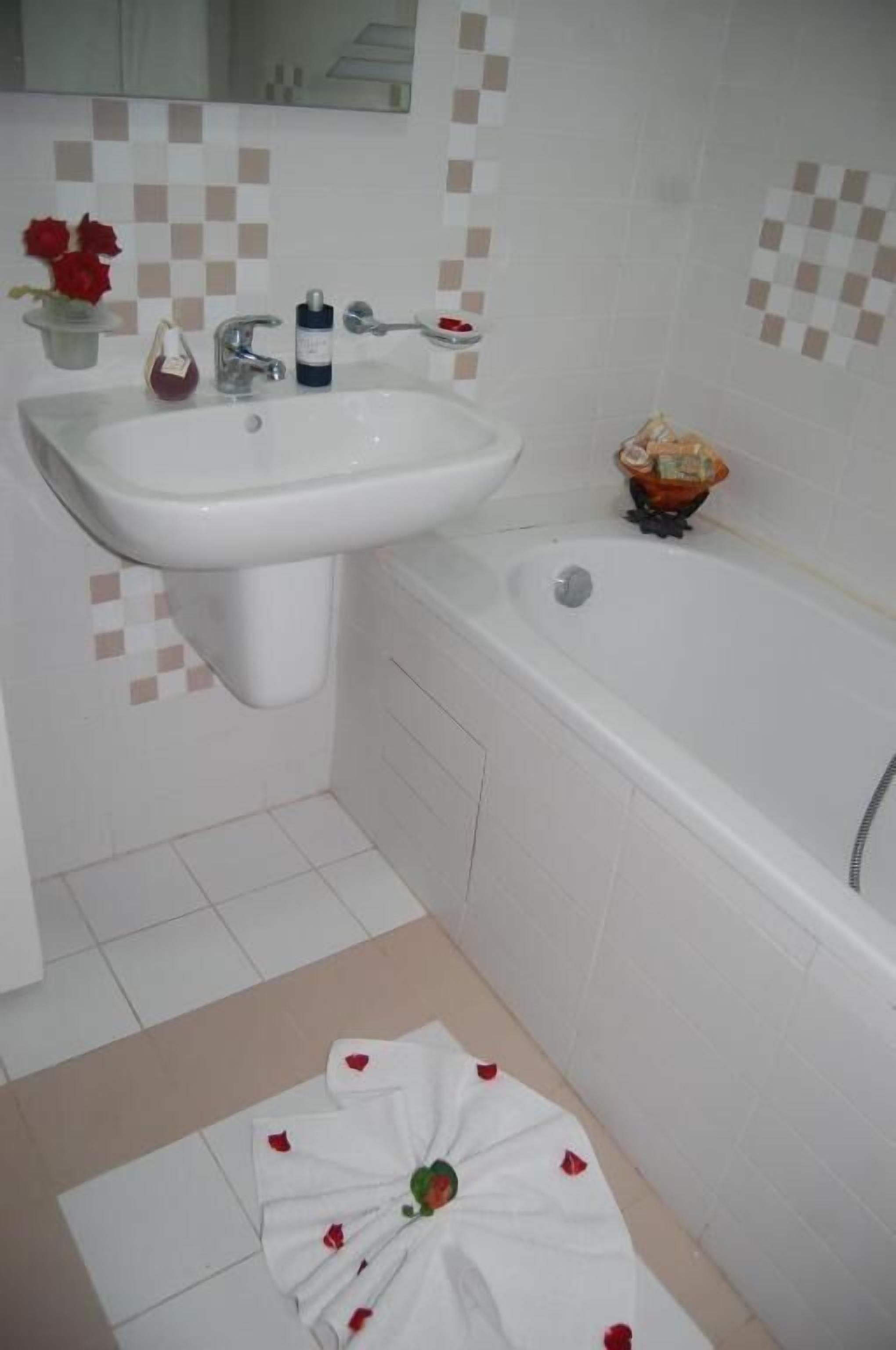 Un baño con lavamanos blanco, bañera y piso de baldosas.