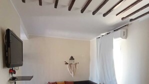 Un salon comprenant un canapé d’angle, un téléviseur à écran plat, une petite table et un plafond avec des poutres en bois.