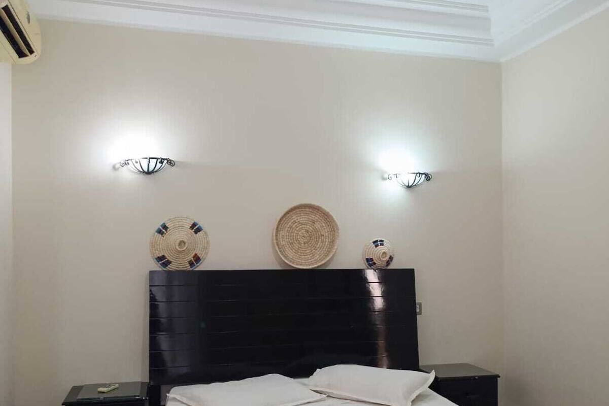 A bedroom with a bed, bedside tables, a headboard, wall-mounted lights, and a decorative plate.