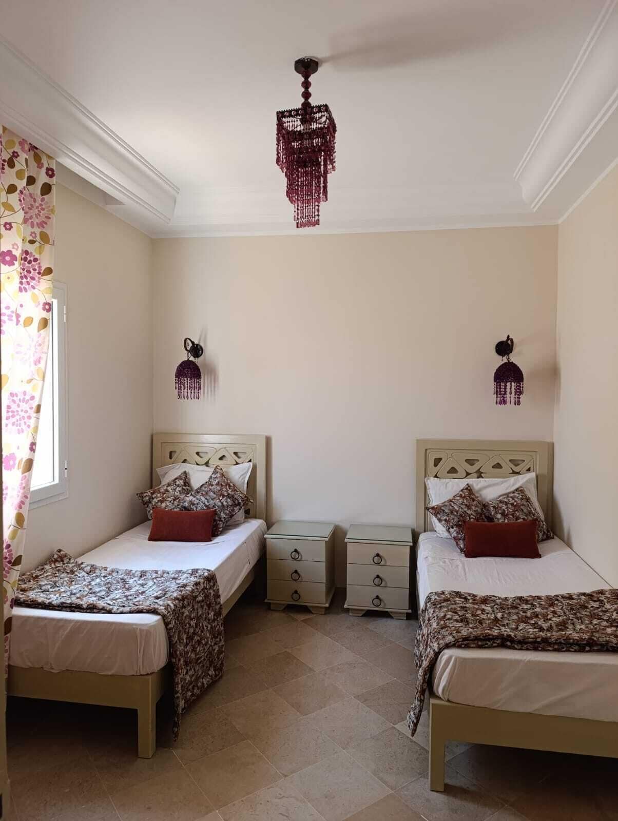 Une chambre avec deux lits, un lustre et une fenêtre avec des rideaux.