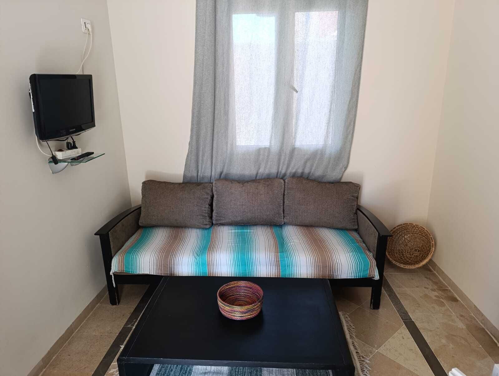 Een kamer met een bank, een aan de muur bevestigde televisie, een gevlochten mand en een salontafel.