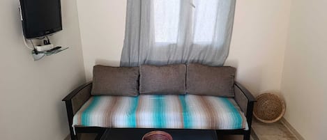 Een kamer met een bank, een aan de muur bevestigde televisie, een gevlochten mand en een salontafel.