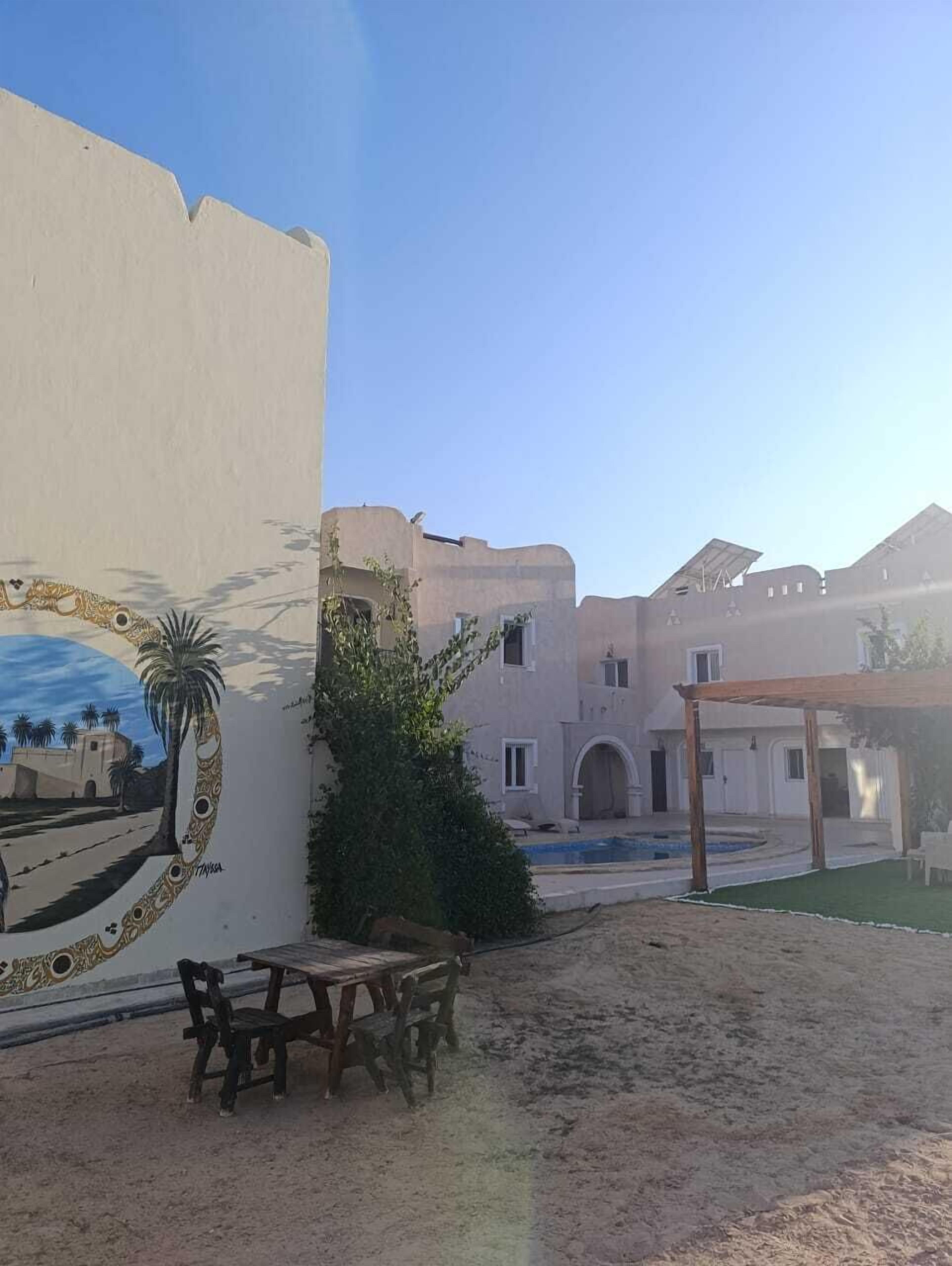 Un cortile con un murale, un tavolo di legno e una zona salotto coperta.