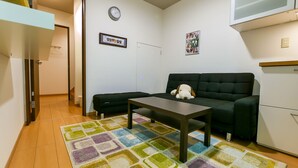 A small living room with a sofa, a coffee table, a colorful rug, a clock, and a framed picture on the wall. - 73BNB House in Chiyozaki (Osaka)