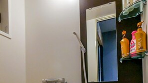 A modern bathroom with a bathtub, a shower, and a toilet. There are toiletries on a shelf above the mirror. - 73BNB House in Chiyozaki (Osaka)