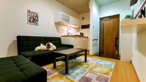 A compact living space with a sofa, a small table, a colorful rug, a kitchenette with a microwave, and a wooden door. - 73BNB House in Chiyozaki (Osaka)