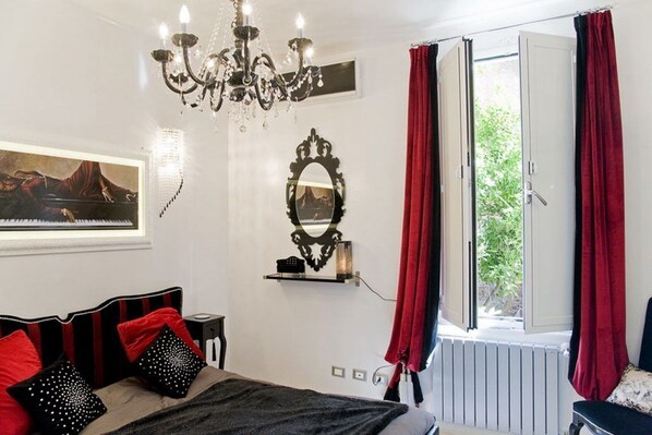 A bedroom with a bed, a chandelier, a mirror, and a window with curtains. - Suite Sweet Rome (Rome)
