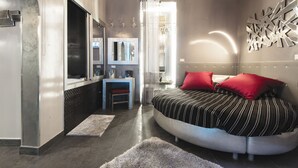 A modern bedroom with a curved bed, a vanity with a mirror, and a chandelier. - Suite Sweet Rome (Rome)