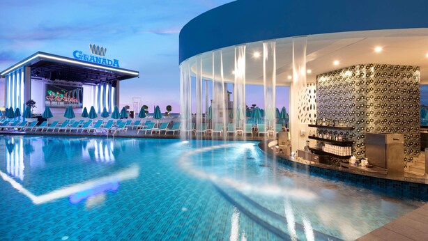 A pool area with lounge chairs and a bar area with a patterned wall. - Granada Luxury Beach - All Inclusive (Alanya)