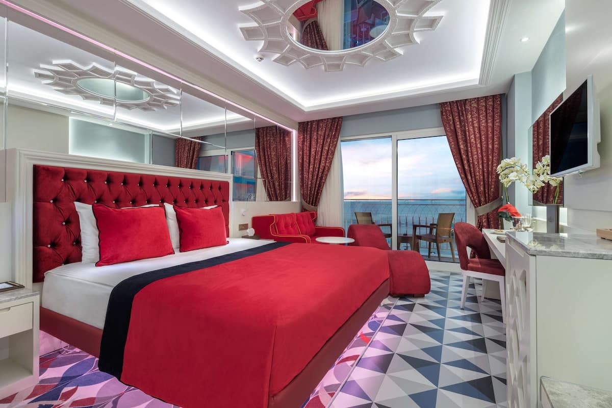 A hotel room with a large bed, a desk, a chair, a TV, and a view of the sea.