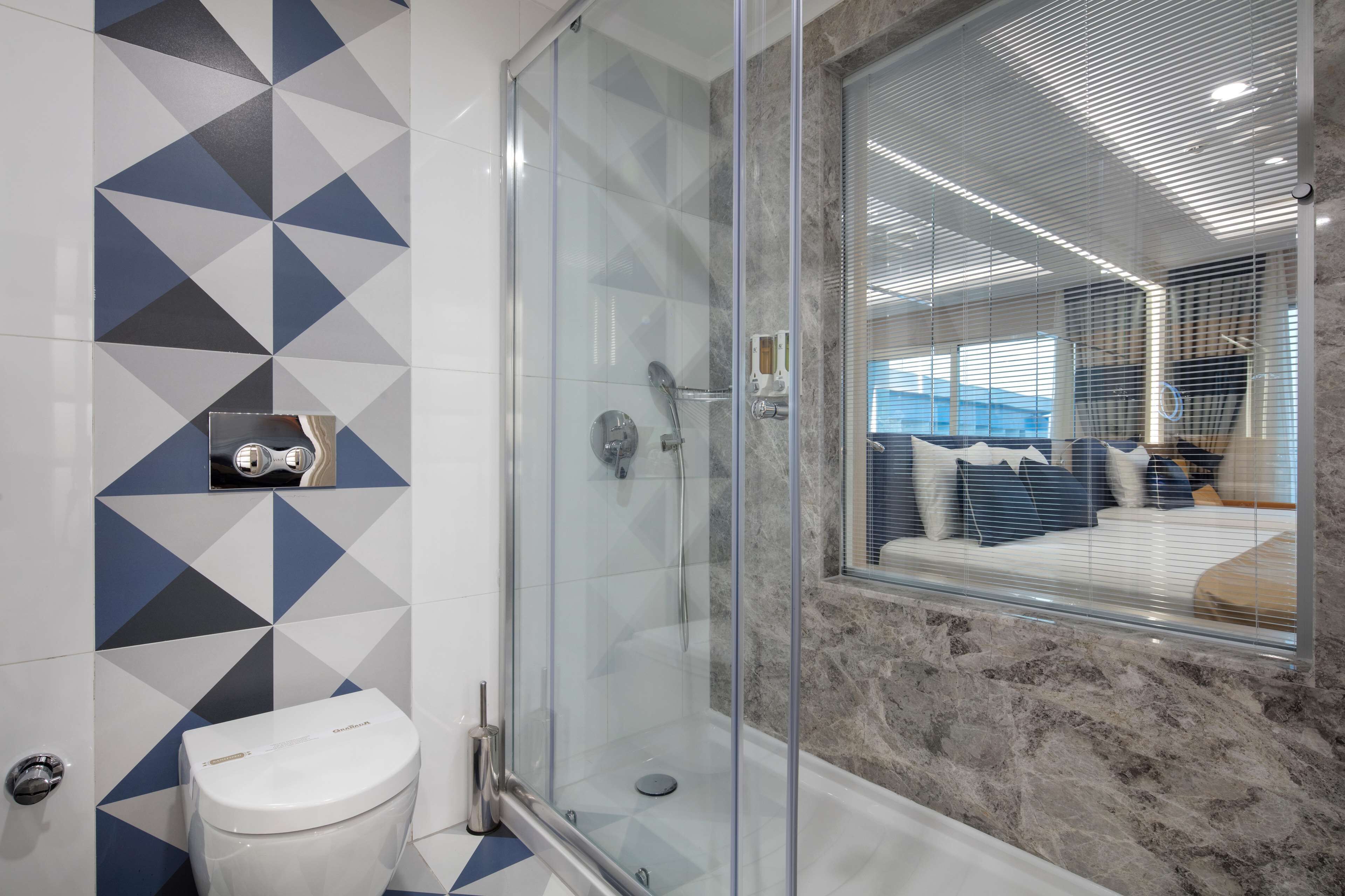 A modern bathroom with a glass-enclosed shower, a toilet, and a marble wall.