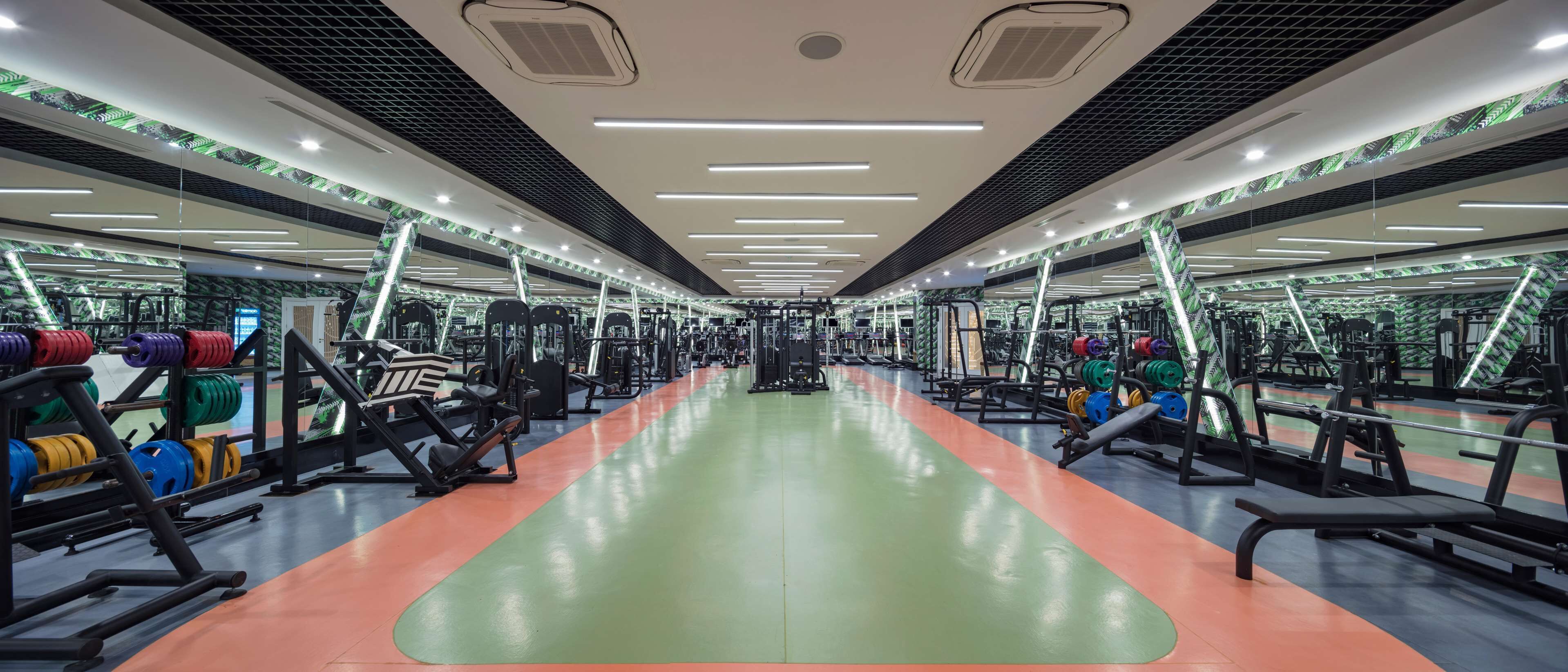 A gym with mirrored walls, weightlifting equipment, and treadmills.