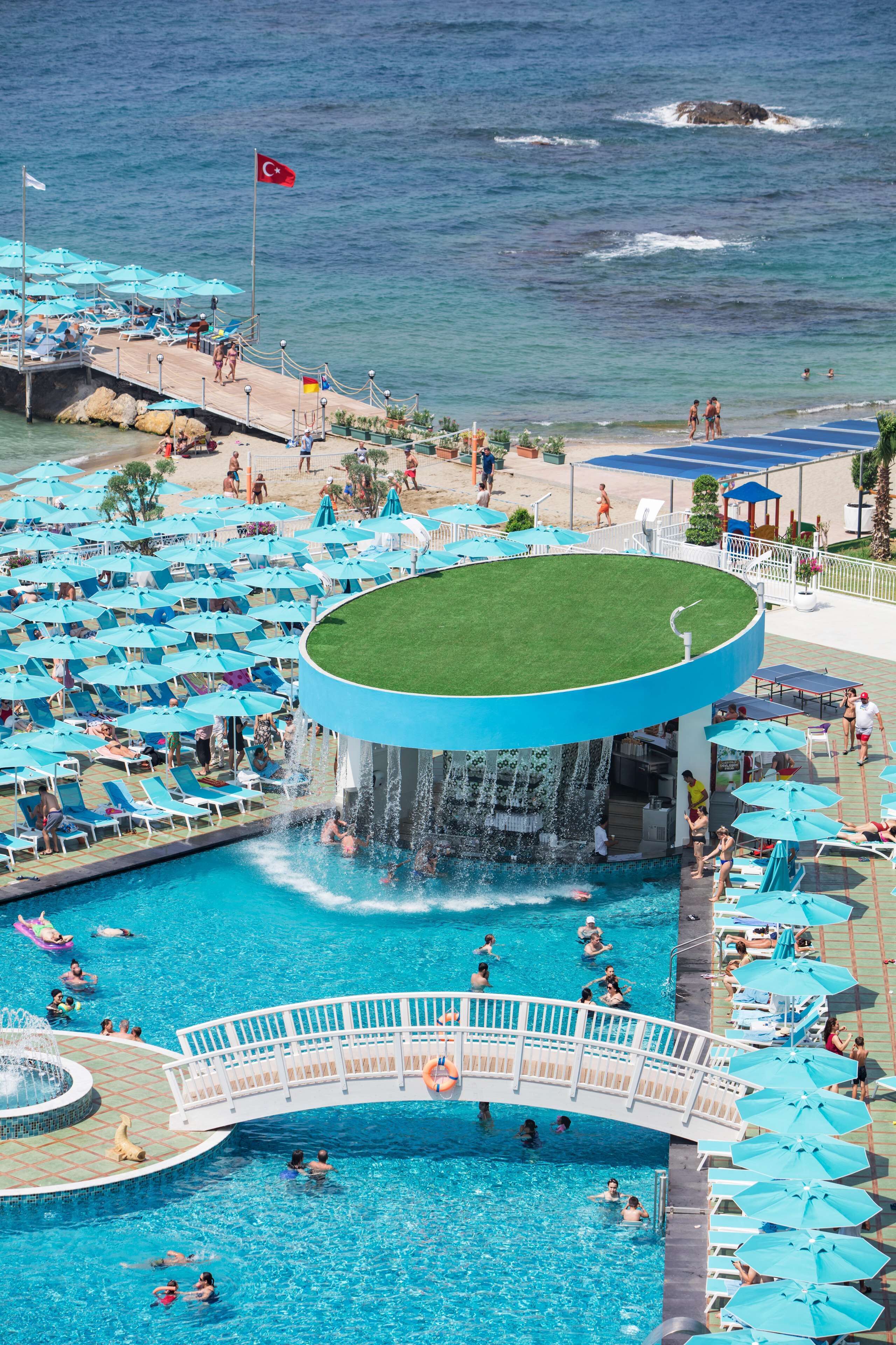 A pool area with multiple blue umbrellas, a water slide, and a flag.