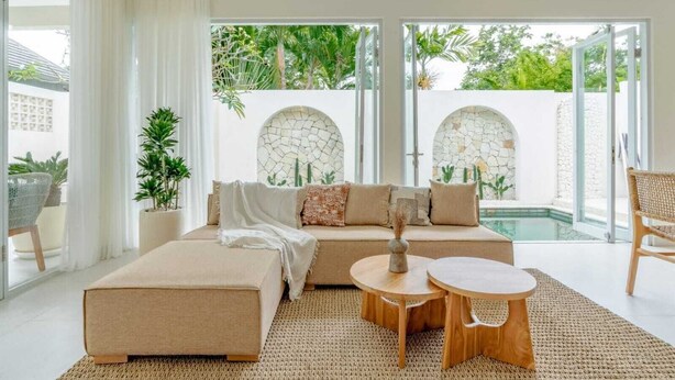 Una sala de estar moderna con un sofá beige, dos mesitas de madera y un ventanal con vistas a una zona de piscina.