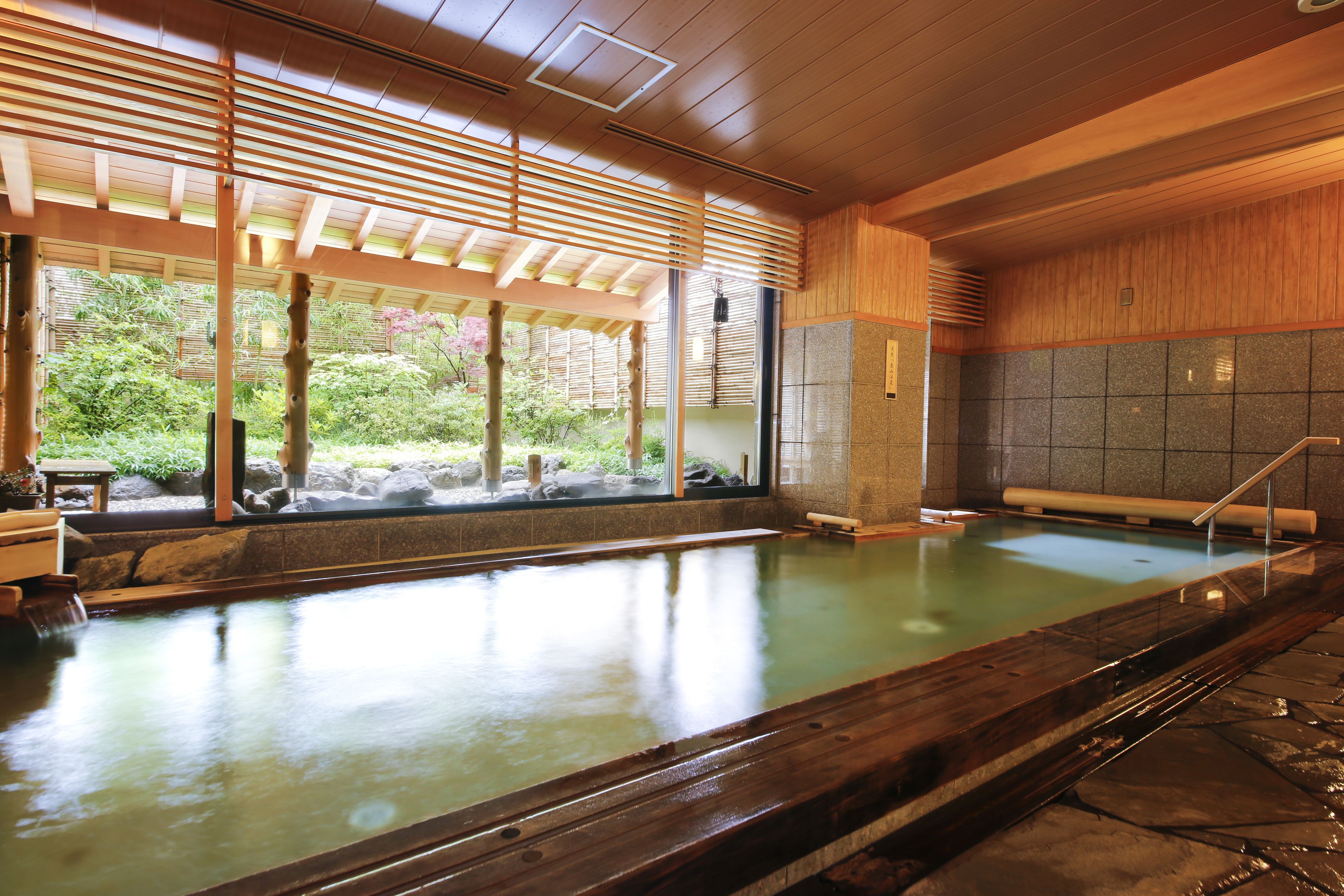 A traditional Japanese onsen with a wooden interior, a stone wall, and a view of greenery outside.