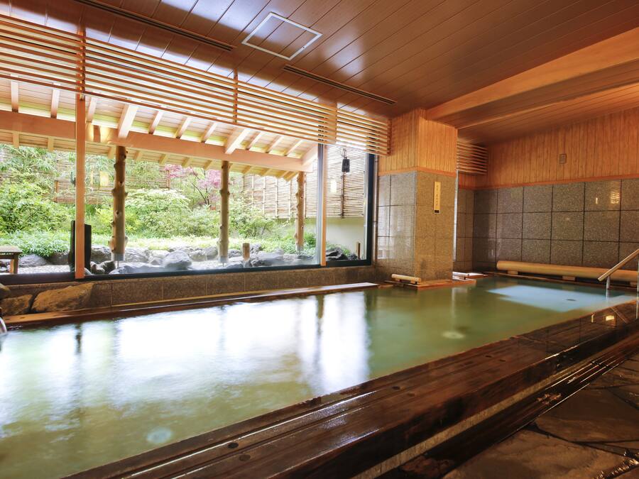 A traditional Japanese onsen with a wooden interior, a stone wall, and a view of greenery outside.