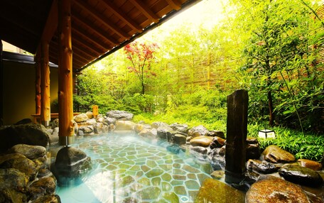 A hot spring area with a stone-tiled pool, wooden pillars, and a bamboo fence.