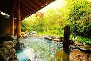 A hot spring area with a stone-tiled pool, wooden pillars, and a bamboo fence. - Kadensho, Arashiyama Onsen, Kyoto - Kyoritsu Resort (Kyoto)