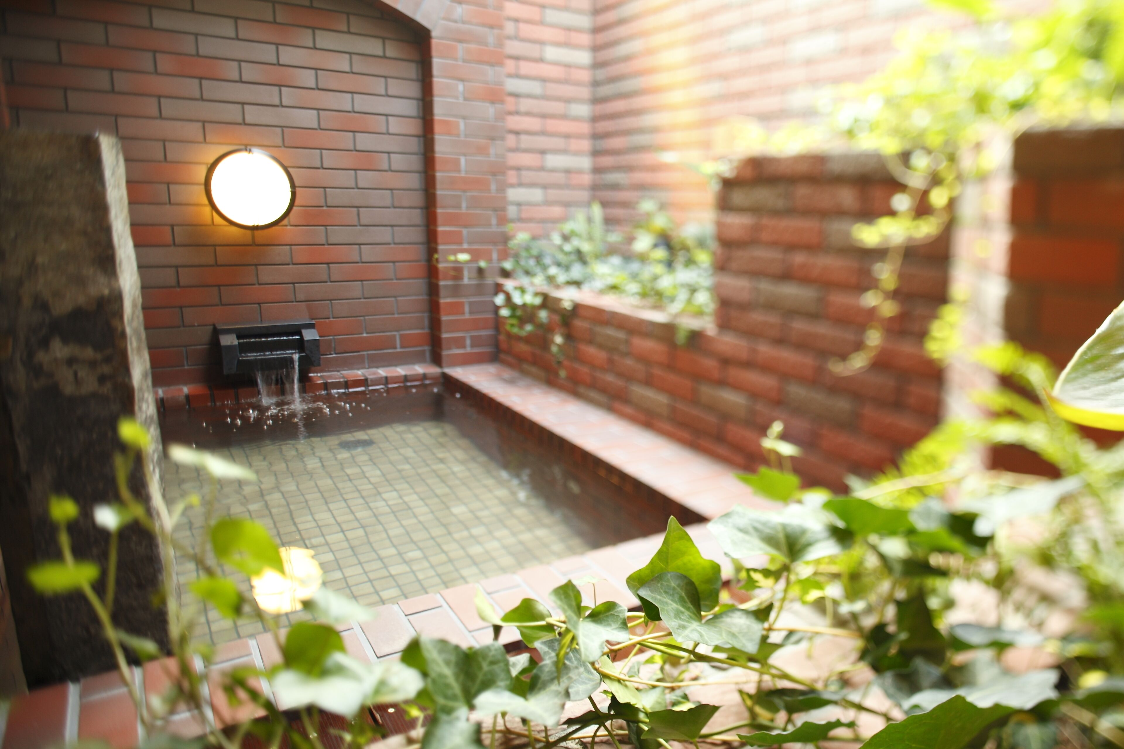 A small outdoor pool area with a brick wall and a water feature.