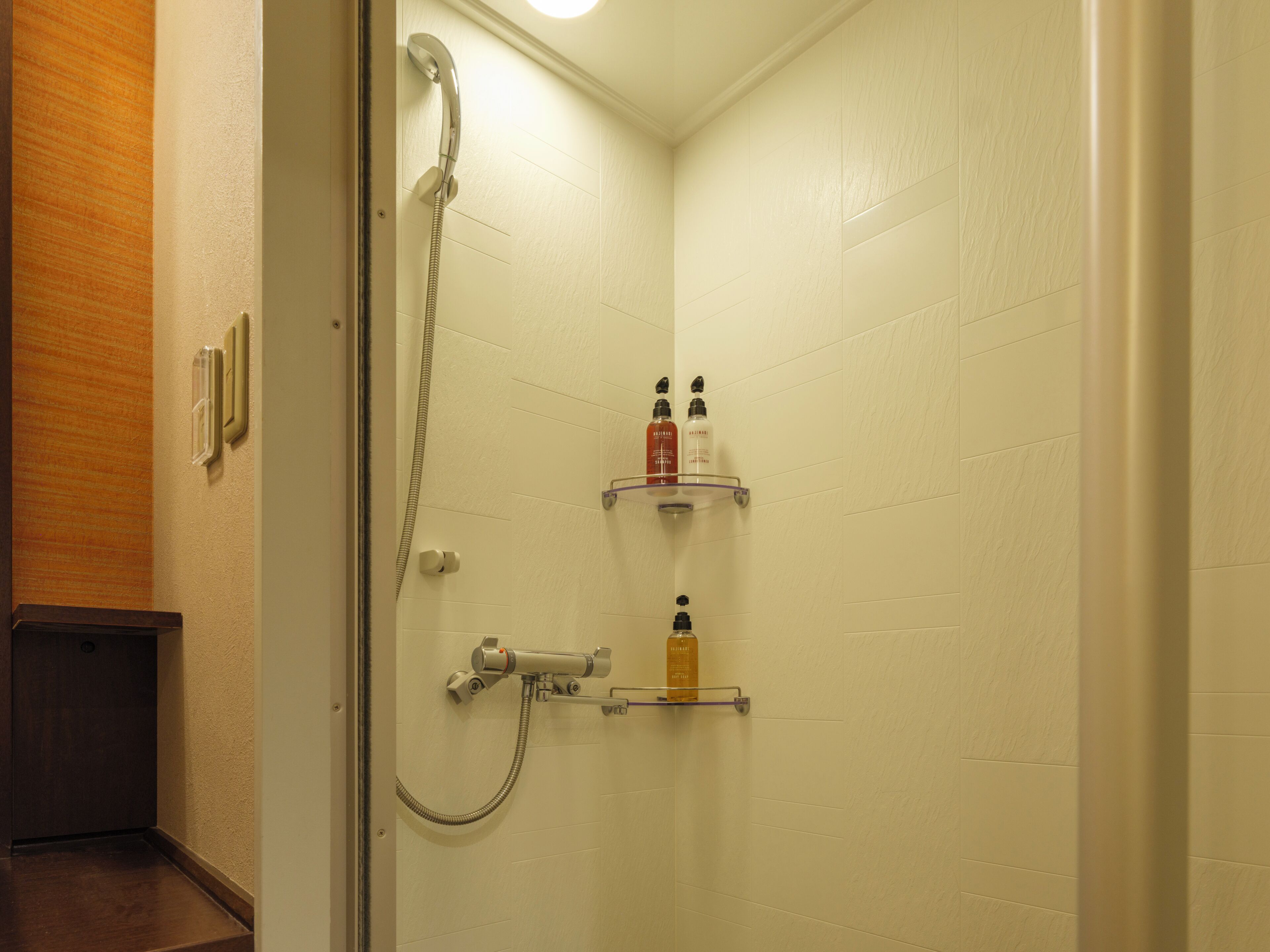 Un baño con ducha, inodoro y dos repisas con artículos de aseo.