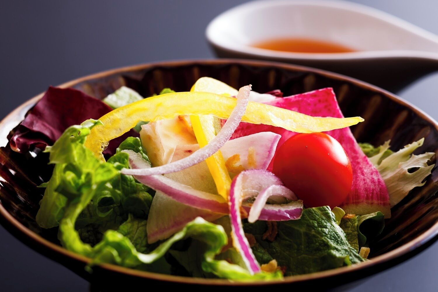 A bowl of salad with various vegetables and a small dish of dressing.
