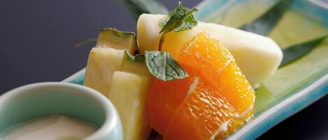 A plate with sliced fruits and a small bowl of sauce.