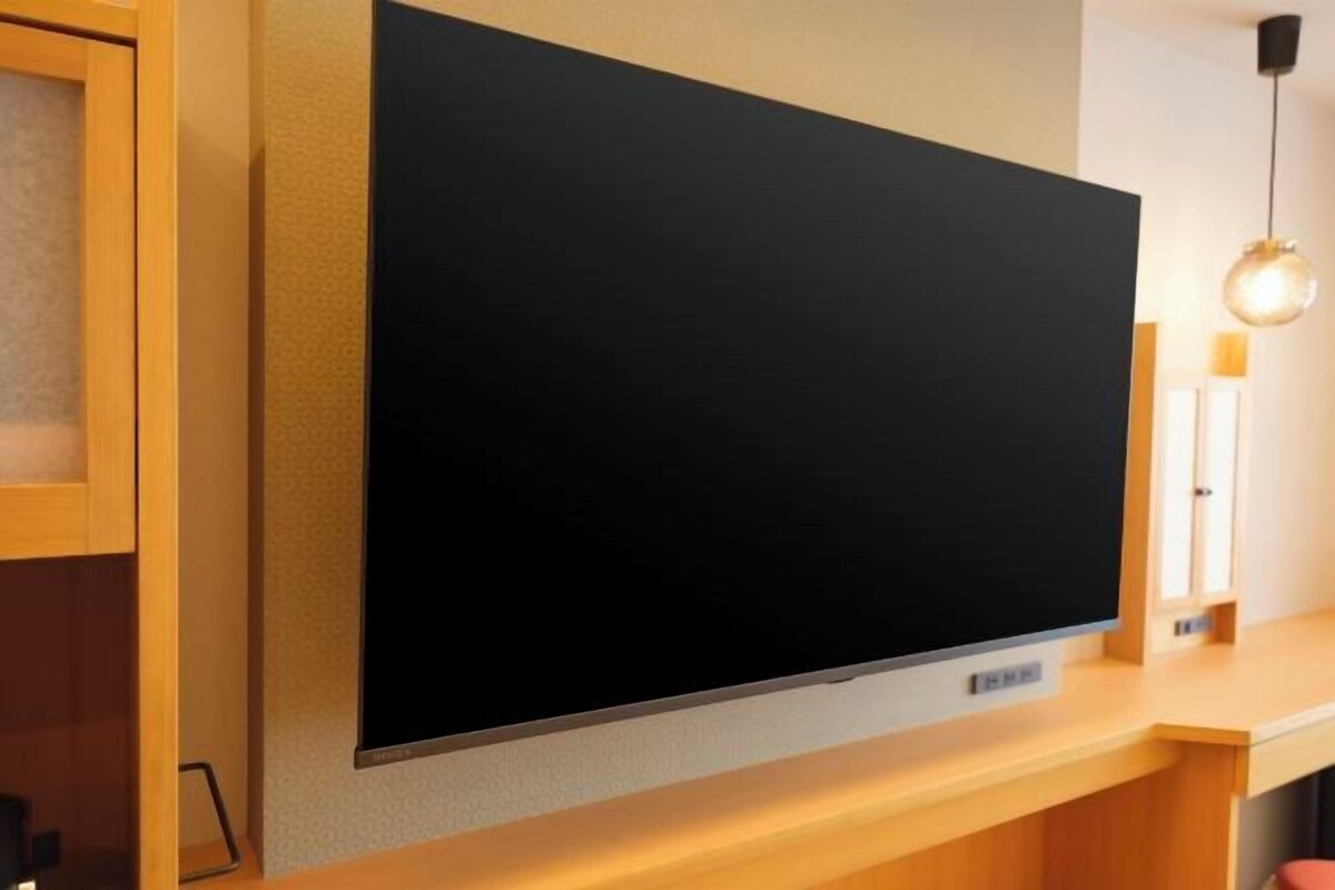 A flat-screen TV mounted on a wall in a room with wooden furniture and a pendant light.
