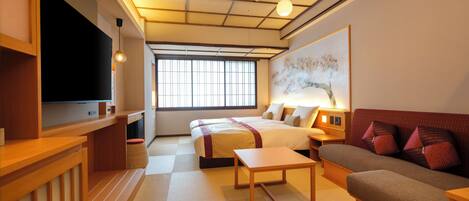 A traditional Japanese-style room with tatami flooring, a futon bed, a wooden desk, a television, and a large window with a view.