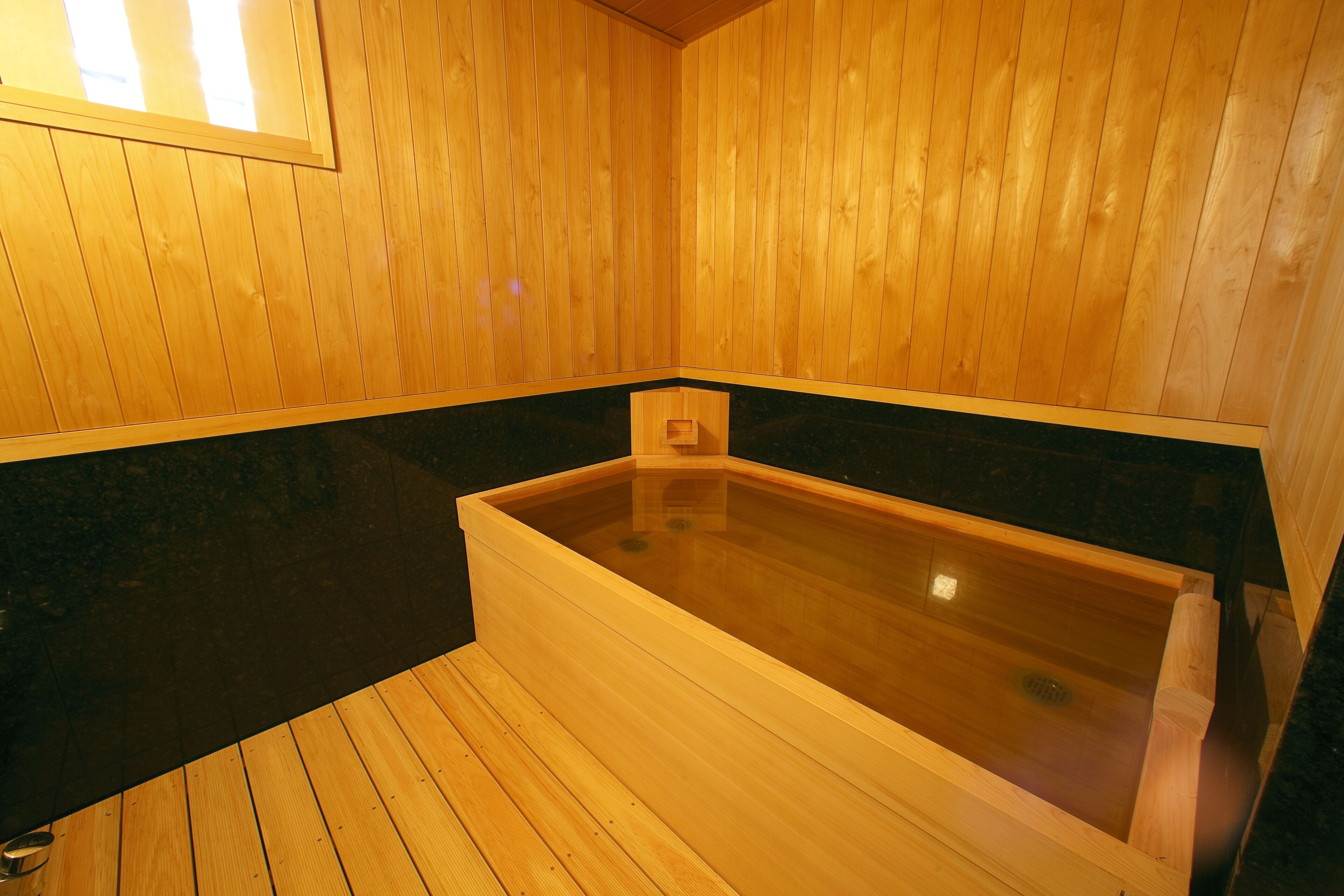 Un sauna en bois doté d’une grande baignoire en bois et d’un plan de travail noir.