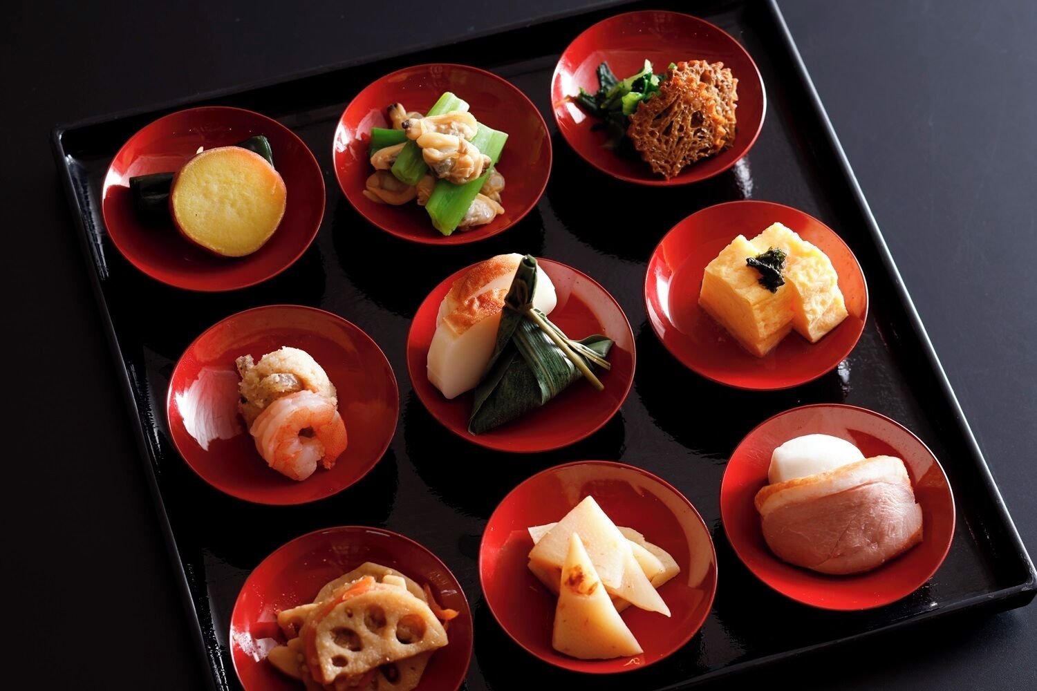 A tray with various Japanese dishes, including sushi, sashimi, and tempura, arranged on red plates.