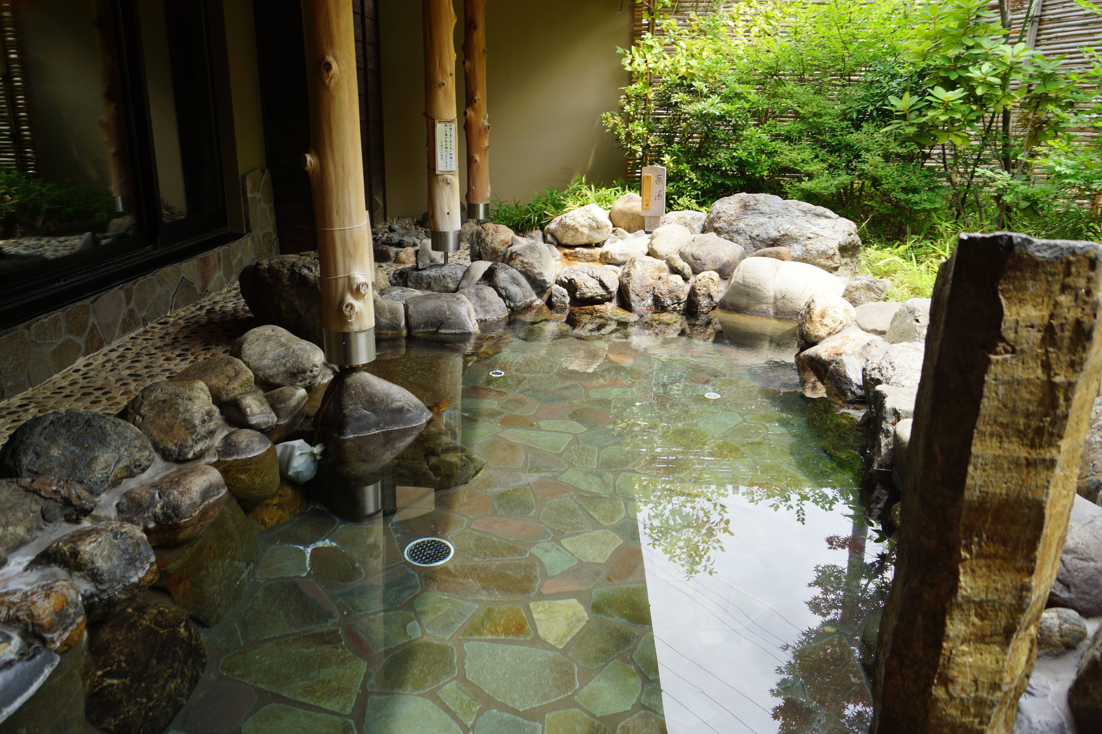 A traditional Japanese garden with a stone pond, bamboo structures, and rocks.