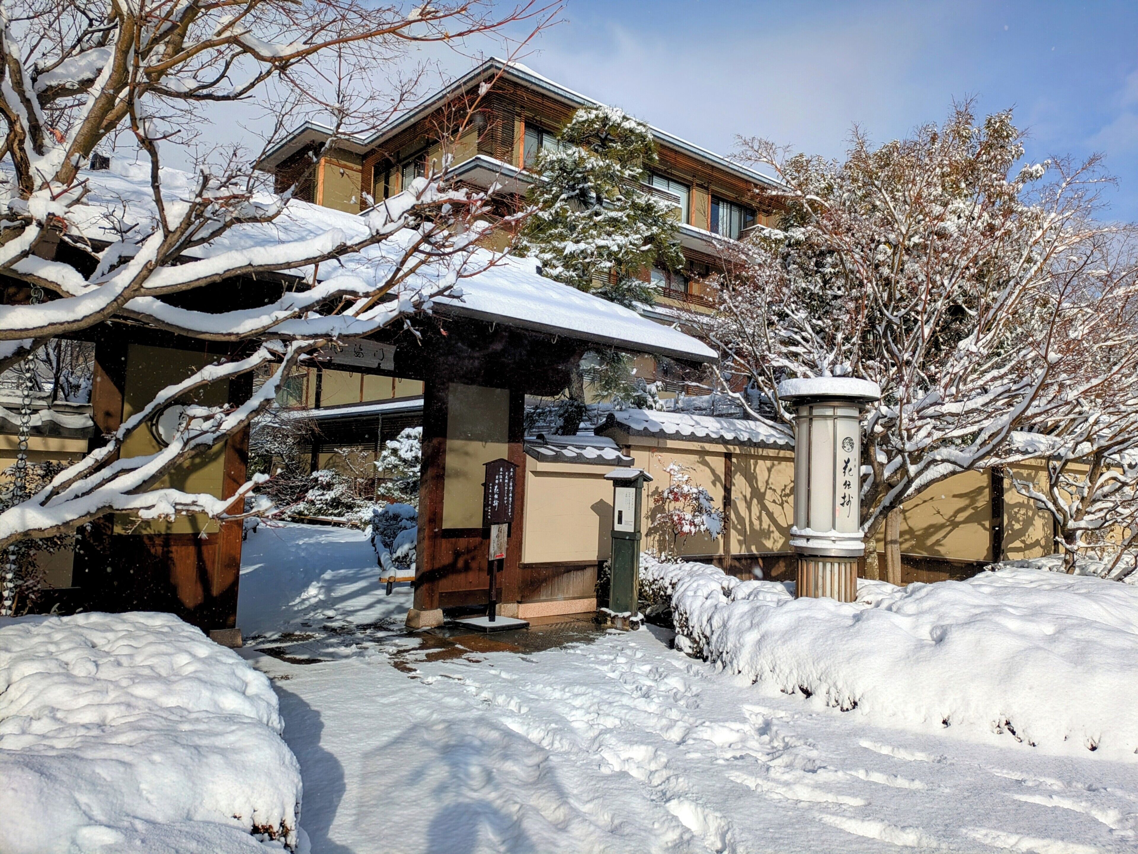 A traditional Japanese house with a snow-covered roof and surrounding garden.