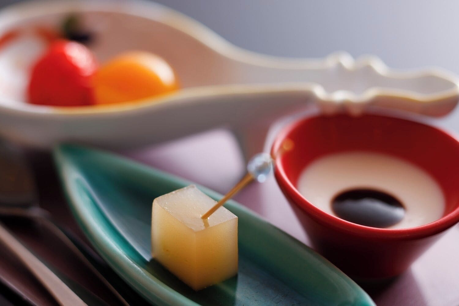 A dessert with a toothpick, a red cup, and a plate with fruits.