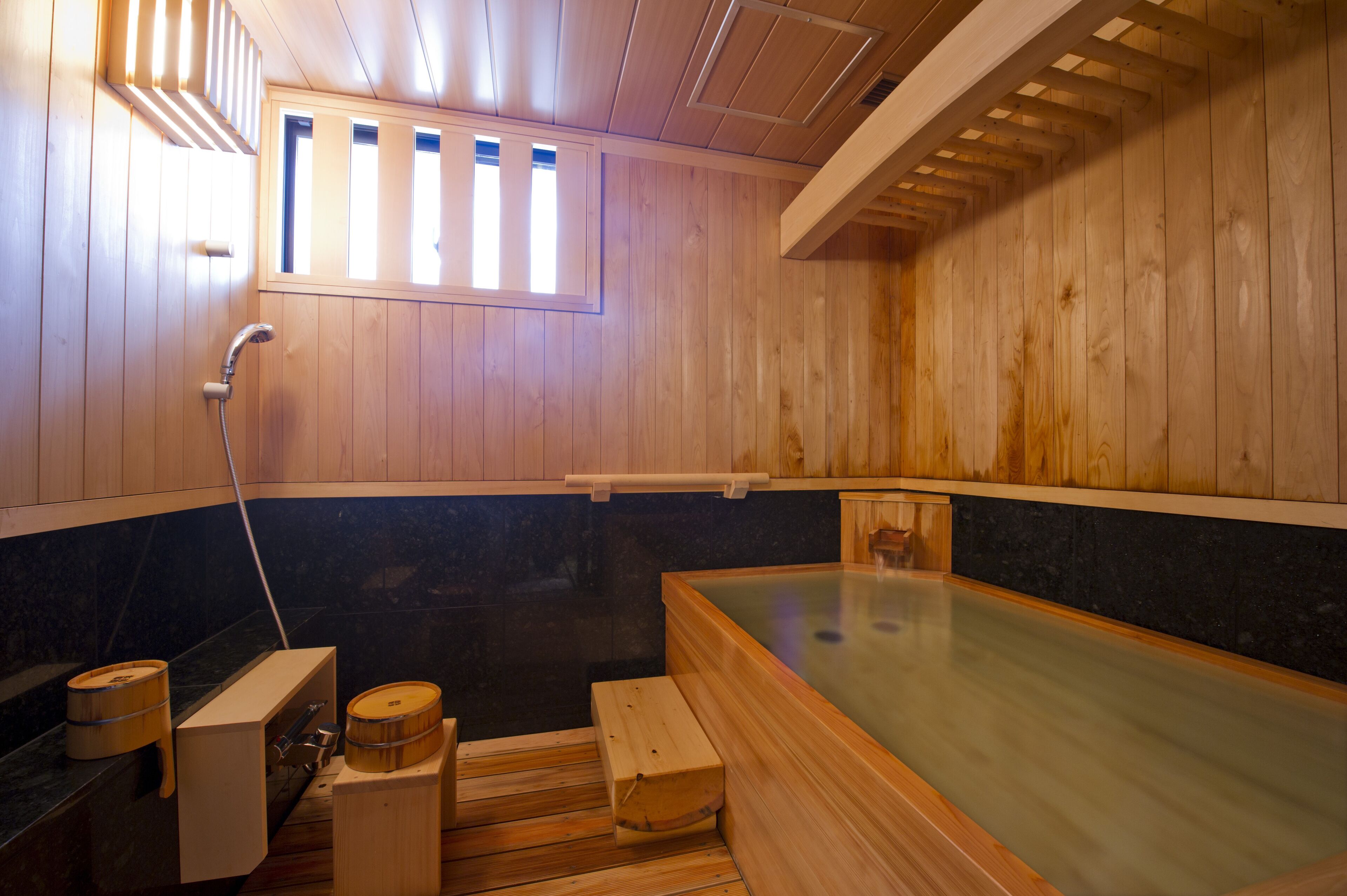 A wooden sauna with a large soaking tub, wooden benches, and a window.