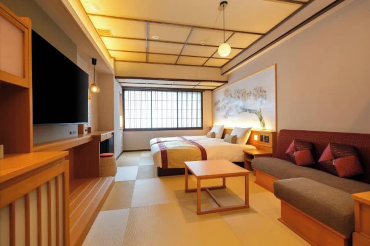 A hotel room with a bed, a sofa, a TV, a painting, and a window.
