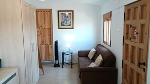 A room with a brown sofa, a wooden wardrobe, a framed picture on the wall, and a standing lamp.
