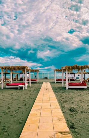 A beach with a tiled walkway leading to beach umbrellas and lounge chairs. - Perla Luxury (Ulcinj)