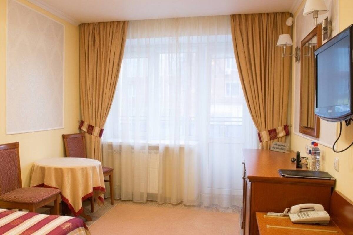 Hotellihuone, jossa on kaksi erillistä sänkyä, pieni pöytä ja tuoli, työpöytä puhelimineen sekä televisio.