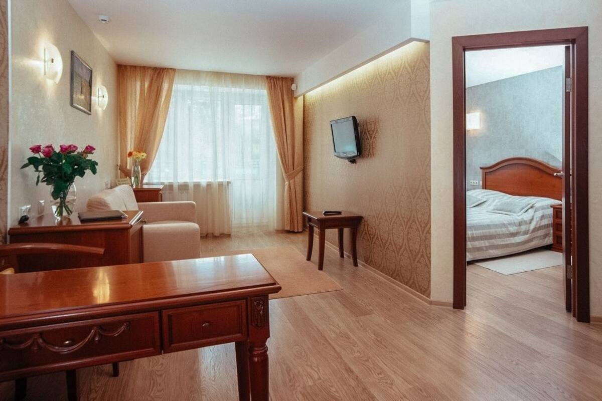 Hotellihuone, jossa on puinen työpöytä, tuoli, yöpöytä, seinälle asennettu televisio ja sängyssä pääty.