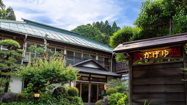 A traditional Japanese building with a wooden exterior, a stone pathway leading to the entrance, and lush greenery surrounding the property. - Kageyu (Isehara)