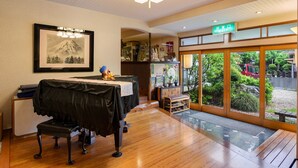 A hotel room with a wooden floor, a dining table with a black tablecloth, a framed picture on the wall, and a view of greenery outside. - Kageyu (Isehara)