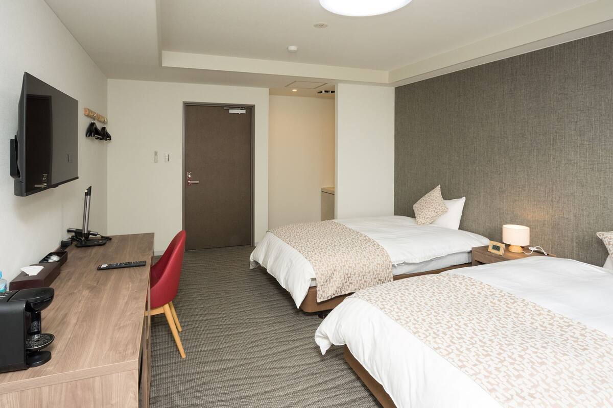 Een hotelkamer met twee bedden, een bureau, een televisie en een deur naar een badkamer.