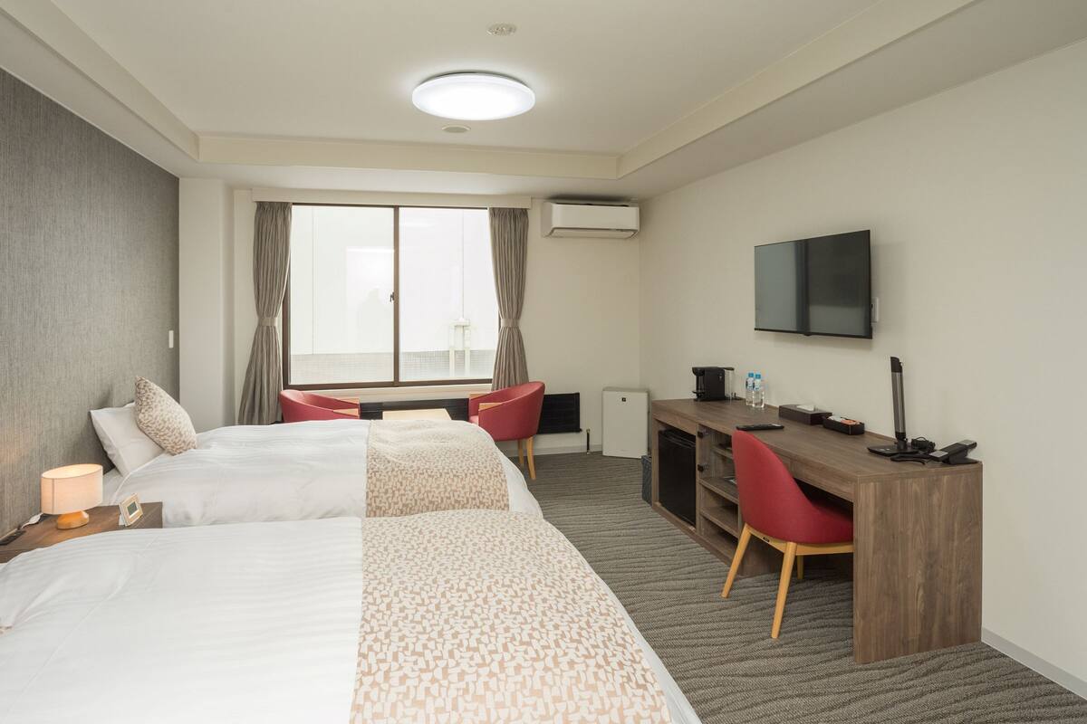 Een hotelkamer met twee bedden, een bureau, een stoel, een televisie en een airconditioning.