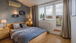 Ein Schlafzimmer mit Wandverkleidung, einem großen Bett, einem Fenster mit Vorhängen, einer Heizung und Blick ins Freie.