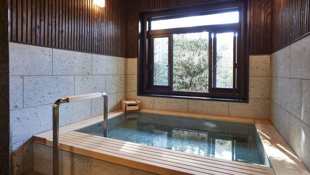 Une salle de spa moderne dotée d’un jacuzzi entouré de parois en verre, de bancs en bois et d’une fenêtre avec des stores.