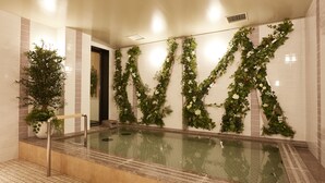 Un espace piscine doté d’un sol carrelé, d’un escalier métallique pour accéder à la piscine et d’un mur décoré de feuillage vert et de fleurs blanches.
