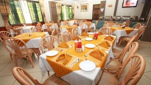 A dining area with multiple tables set for meals, each with white tablecloths, orange napkins, and basic tableware.