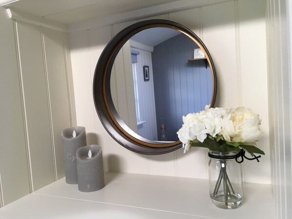 A bathroom vanity with a round mirror, two candles, and a vase with white flowers. - SHEPHERD'S HUT (DELUXE). Beautiful 1 bedroom, with patio, ideal for couples. (Fordingbridge)