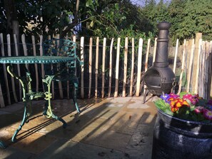 A patio with a metal table and chairs, a stone barbecue grill, and a wooden fence. - SHEPHERD'S HUT (DELUXE). Beautiful 1 bedroom, with patio, ideal for couples. (Fordingbridge)